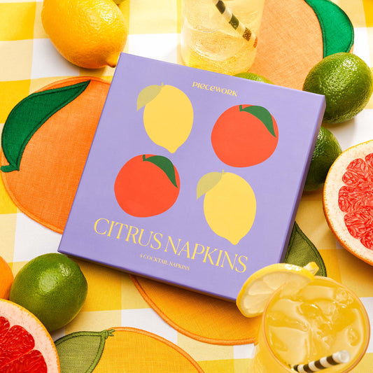 Piecework Citrus Napkins gift box with orange and lemon napkins styled with citrus fruit and iced drinks.